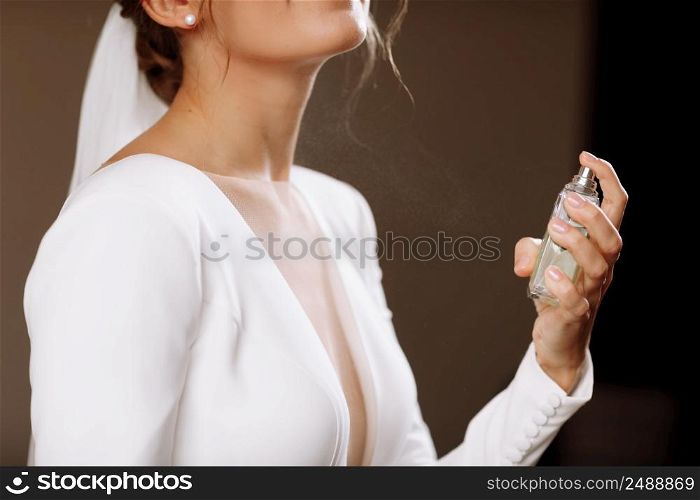 A woman in a white wedding dress gown with a neckline holds a bottle with perfume and splashes on her neck. Morning of the bride in the house, hands without face. A woman in a white wedding dress gown with a neckline holds a bottle with perfume and splashes on her neck. Morning of the bride in the house, hands without face.
