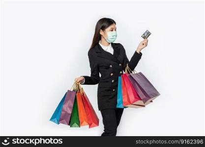 A woman in black and wearing a mask walks shopping, carries credit cards, and lots of bags.