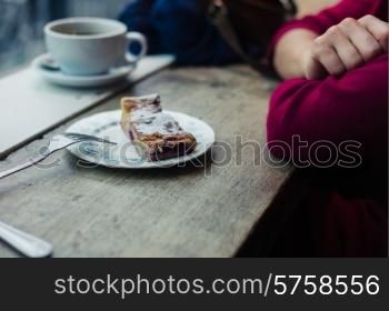 A woman is having coffee and cake by a window in a cafe