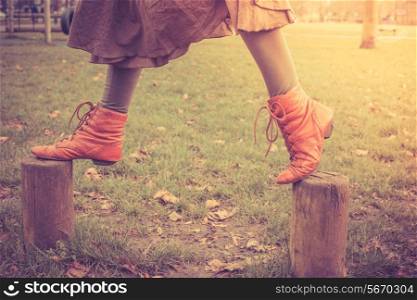 A woman is playfully wlking on some small wooden posts in the park