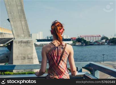 A woman is standing on a bridge and is looking at the river in a city