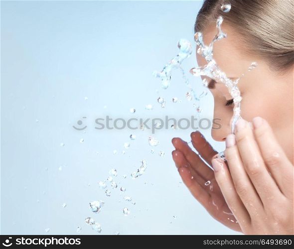 A woman is washing her face with cold water, cleaning skin after makeup, using anti acne or anti aging agent, pampering and beauty care concept, over blue clear background. Fresh start