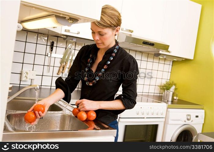 A woman is washing tomatoes in the sink at home in the kitchen.