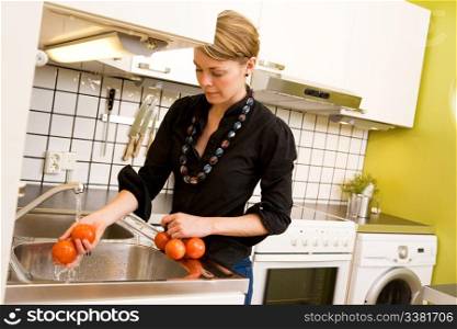 A woman is washing tomatoes in the sink at home in the kitchen.