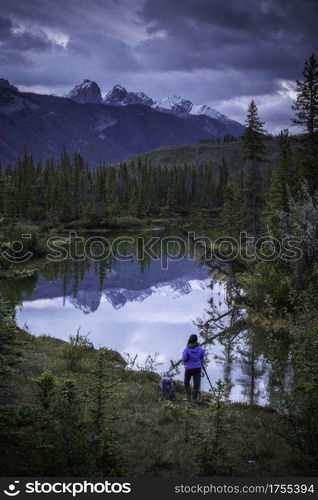 A woman lines up her photograph at a mirror like creek reflection on a blue morning in Jasper national Park.