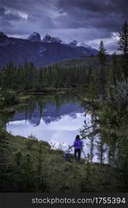 A woman lines up her photograph at a mirror like creek reflection on a blue morning in Jasper national Park.
