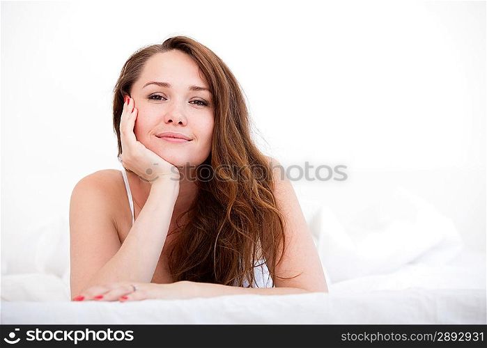 A woman lying at the end of the bed looking forward, Her hand against her chin with her other arm on the bed.