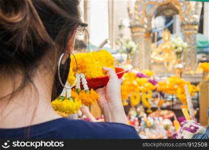 A woman make ceremonial offerings from floral garlands at the Erawan Shrine in Bangkok, Thailand.