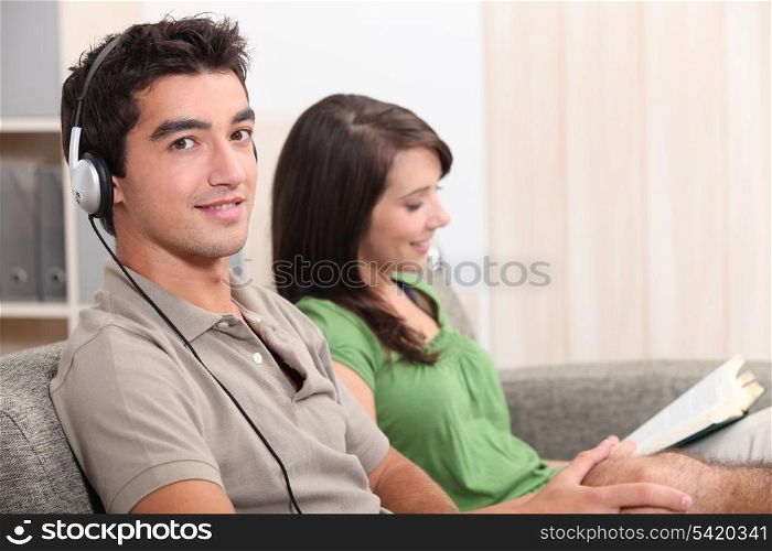 a woman reading and a young man listening music on a couch