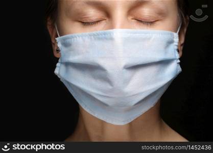 a woman&rsquo;s face in a medical mask on black background, an outbreak of coronavirus infection and protection from it. close- up, Studio portrait on a dark. copy space, look at the camera.. a woman&rsquo;s face in a medical mask on black background, an outbreak of coronavirus infection and protection from it. close- up, Studio portrait on a dark. copy space, look at the camera