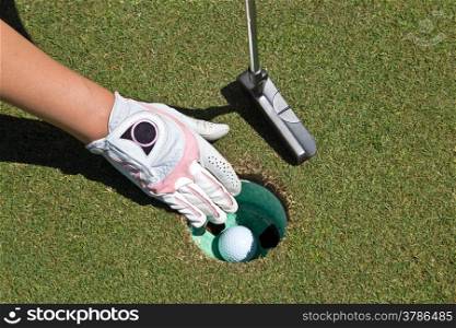 A woman&rsquo;s gloved hand, putter and golf ball in the cup