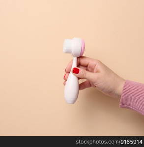 A woman&rsquo;s hand holds a plastic brush for face and body on a beige background