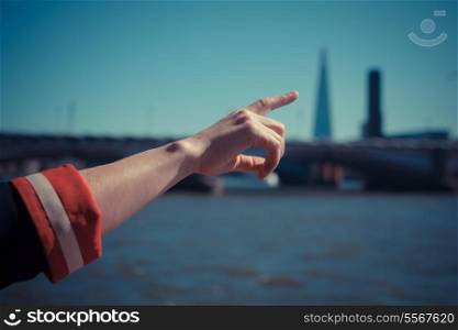A woman&rsquo;s hand is pointing at a skyscraper by the river
