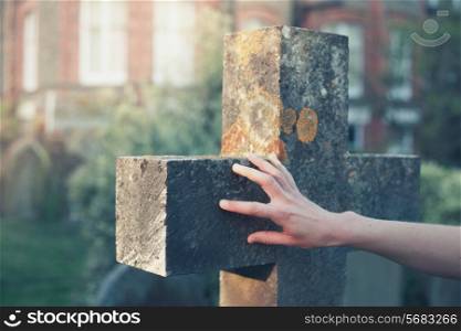 A woman&rsquo;s hand is touching a gravestone at sunset
