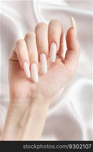 A woman’s hands with a manicure on them, the nails are painted in a white color. White silk background