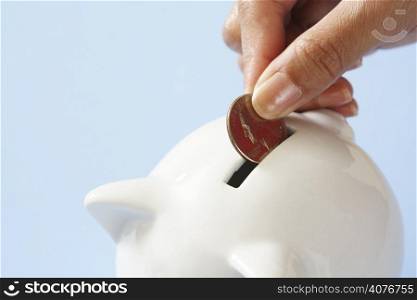 A woman saving a coin into a piggy bank