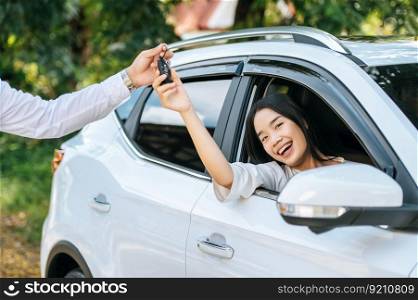 A woman sits in a car and holds out her hand to receive the car keys.