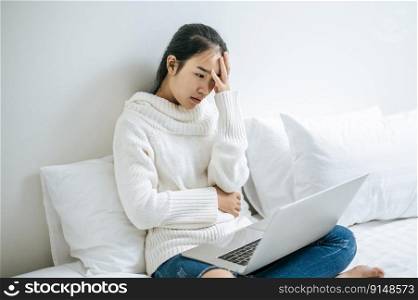 A woman sitting in bed playing a laptop and having stress.