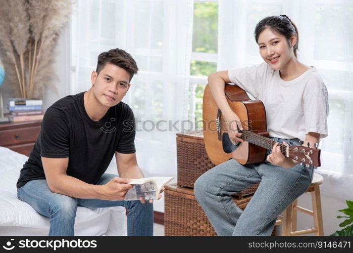 A woman sitting play the guitar and a man holding a book and singing.