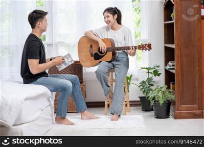 A woman sitting play the guitar and a man holding a book and singing.