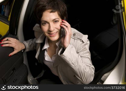 A woman smiling as she gets out of taxi cab simultaniously talking on cell phone