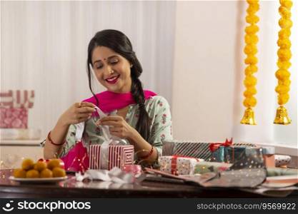A woman tying ribbon to wrap gift amidst presents,sweets,Diwali light and festive garland decoration.