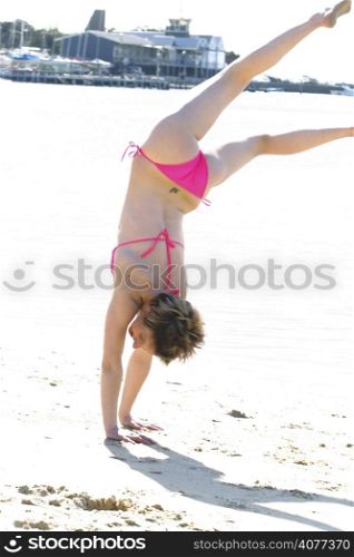 A woman upside down doing a handstand at the beach. Fun free can happy.