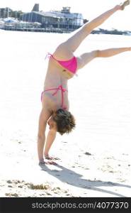 A woman upside down doing a handstand at the beach. Fun free can happy.
