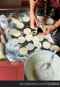 A woman using a rolling pin and a glass prepares round dough blanks for modeling dumplings in Ukrainian national cuisine.. A woman using a rolling pin and a glass prepares a dough for making dumplings.