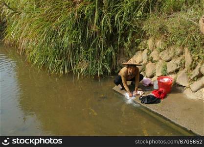 A woman washes her clothing in a river in China.