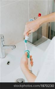 A woman washing his electrical toothbrush pieces and putting teeth cream over it
