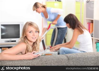 a woman watching tv, a woman doing computer and another one vacuuming