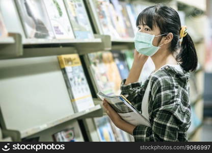 A woman wearing a mask and searching for books in the library.