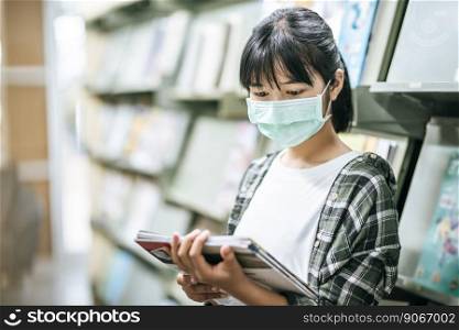 A woman wearing a mask and searching for books in the library.