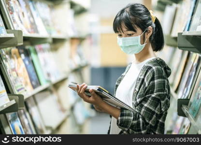 A woman wearing a mask and searching for books in the library.