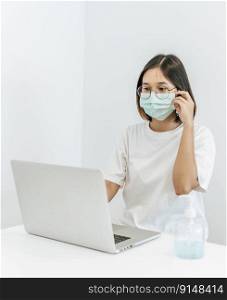 A woman wearing a mask playing a laptop and having a bottle of handwashing gel.