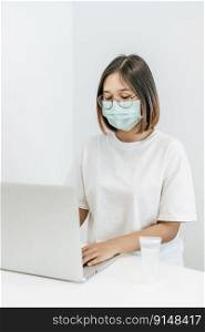 A woman wearing a mask playing a laptop and having a bottle of handwashing gel.