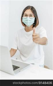 A woman wearing a mask playing a laptop and thumbs up.