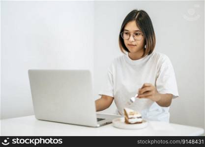 A woman wearing a mask playing on a laptop and having a cake on the plate.