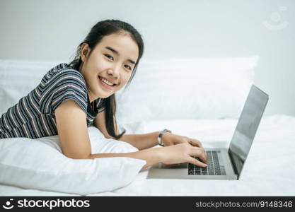 A woman wearing a striped shirt on the bed and playing a laptop.