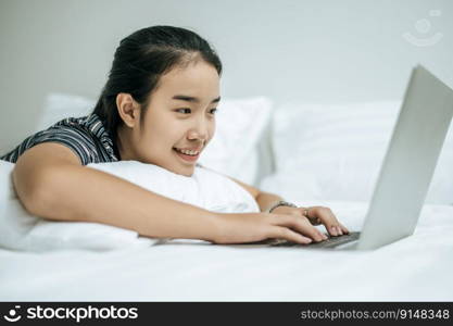 A woman wearing a striped shirt on the bed and playing a laptop.