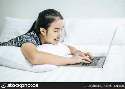 A woman wearing a striped shirt on the bed and playing a laptop.