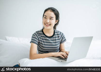 A woman wearing a striped shirt on the bed and playing laptop happily.