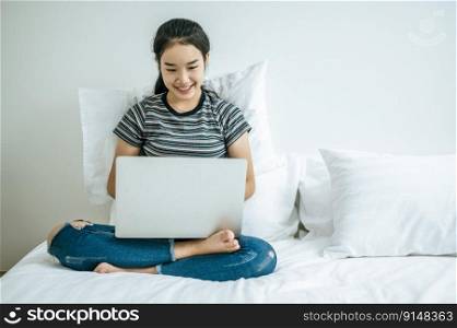 A woman wearing a striped shirt on the bed and playing laptop happily.