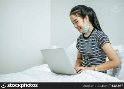 A woman wearing a striped shirt on the bed and playing laptop happily.