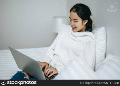 A woman wearing a white shirt on the bed and playing laptop happily.