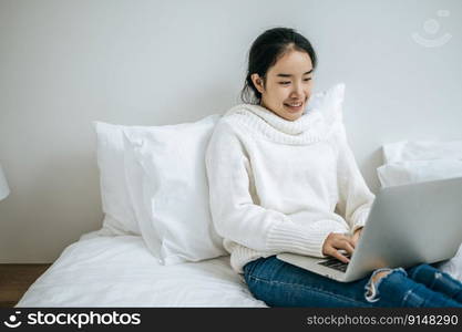 A woman wearing a white shirt on the bed and playing laptop happily.