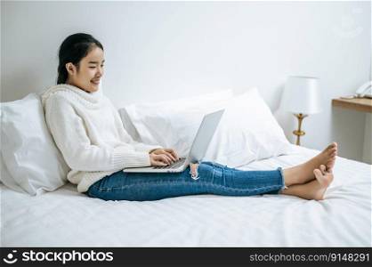 A woman wearing a white shirt on the bed and playing laptop happily.