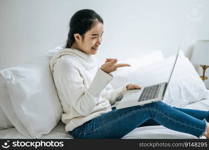 A woman wearing a white shirt on the bed and playing laptop happily.