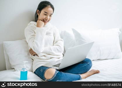 A woman wearing a white shirt on the bed and playing laptop happily.